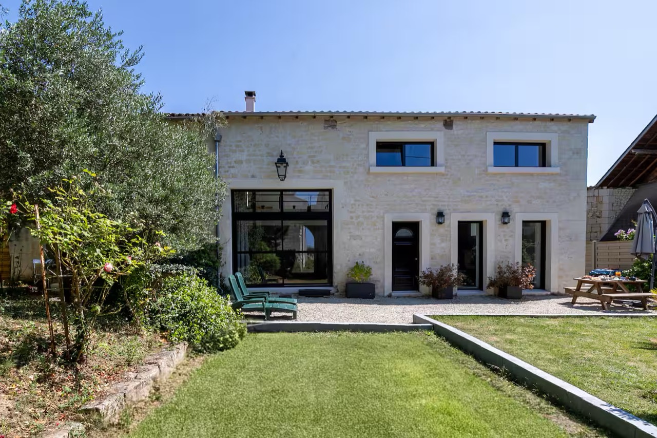 Façade en pierre de la maison, terrasse gravillonnée, transats et jardin