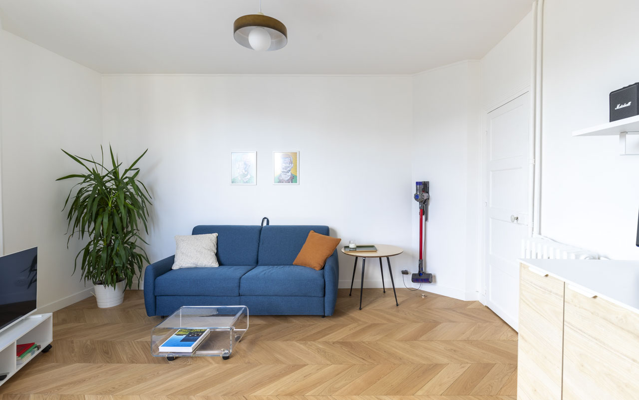 Séjour lumineux avec parquet à chevrons, canapé bleu et grande fenêtre